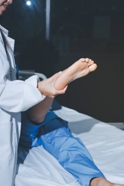 Hastane odasında yaralı bir kadının ayak bileğini inceleyen ve destekleyen doktor, burkulma ya da kırık için tıbbi yardım ve tedavi sunuyor.