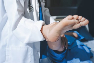 Hastane odasında yaralı bir kadının ayak bileğini inceleyen ve destekleyen doktor, burkulma ya da kırık için tıbbi yardım ve tedavi sunuyor.