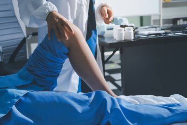 Hastane odasında yaralı bir kadının ayak bileğini inceleyen ve destekleyen doktor, burkulma ya da kırık için tıbbi yardım ve tedavi sunuyor.