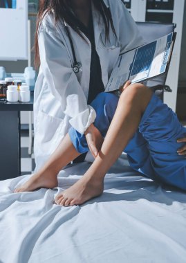 Hastane odasında yaralı bir kadının ayak bileğini inceleyen ve destekleyen doktor, burkulma ya da kırık için tıbbi yardım ve tedavi sunuyor.