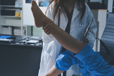 Hastane odasında yaralı bir kadının ayak bileğini inceleyen ve destekleyen doktor, burkulma ya da kırık için tıbbi yardım ve tedavi sunuyor.