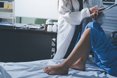 Hastane odasında yaralı bir kadının ayak bileğini inceleyen ve destekleyen doktor, burkulma ya da kırık için tıbbi yardım ve tedavi sunuyor.