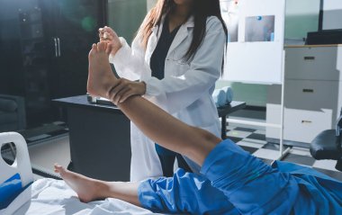 Hastane odasında yaralı bir kadının ayak bileğini inceleyen ve destekleyen doktor, burkulma ya da kırık için tıbbi yardım ve tedavi sunuyor.