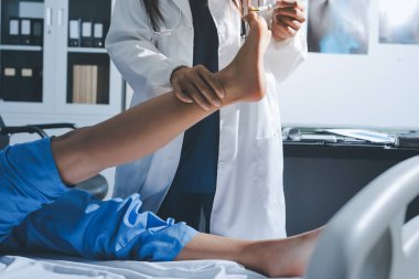 Hastane odasında yaralı bir kadının ayak bileğini inceleyen ve destekleyen doktor, burkulma ya da kırık için tıbbi yardım ve tedavi sunuyor.