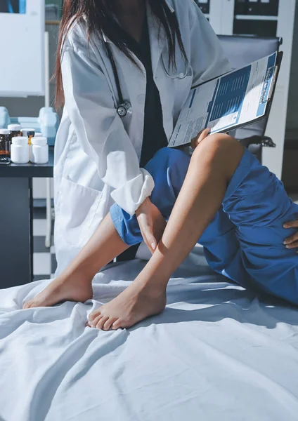 Hastane odasında yaralı bir kadının ayak bileğini inceleyen ve destekleyen doktor, burkulma ya da kırık için tıbbi yardım ve tedavi sunuyor.