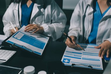 Two doctors and a female nurse meet at a table in the hospital, collaborating on medical tasks using laptops and computers