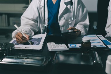 Two doctors and a female nurse meet at a table in the hospital, collaborating on medical tasks using laptops and computers