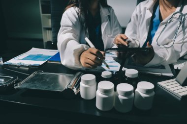 Two doctors and a female nurse meet at a table in the hospital, collaborating on medical tasks using laptops and computers