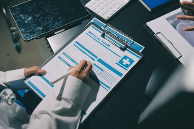 Two doctors and a female nurse meet at a table in the hospital, collaborating on medical tasks using laptops and computers