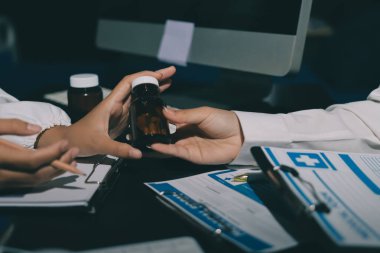 Two doctors and a female nurse meet at a table in the hospital, collaborating on medical tasks using laptops and computers