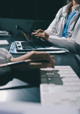 Two doctors and a female nurse meet at a table in the hospital, collaborating on medical tasks using laptops and computers