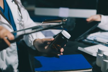 Two doctors and a female nurse meet at a table in the hospital, collaborating on medical tasks using laptops and computers