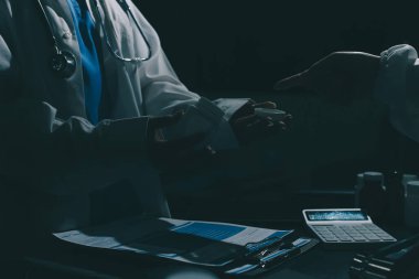 Two doctors and a female nurse meet at a table in the hospital, collaborating on medical tasks using laptops and computers