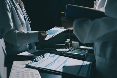 Two doctors and a female nurse meet at a table in the hospital, collaborating on medical tasks using laptops and computers