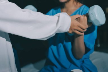 Fizyoterapist, halter egzersizinde bir kadına yardım ediyor.