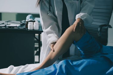 Hastane odasında yaralı bir kadının ayak bileğini inceleyen ve destekleyen doktor, burkulma ya da kırık için tıbbi yardım ve tedavi sunuyor.