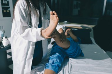 Hastane odasında yaralı bir kadının ayak bileğini inceleyen ve destekleyen doktor, burkulma ya da kırık için tıbbi yardım ve tedavi sunuyor.