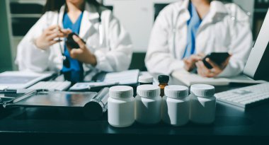 Two doctors and a female nurse meet at a table in the hospital, collaborating on medical tasks using laptops and computers