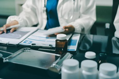 Two doctors and a female nurse meet at a table in the hospital, collaborating on medical tasks using laptops and computers