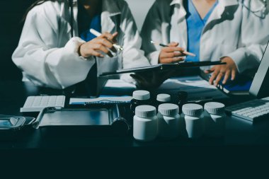 Two doctors and a female nurse meet at a table in the hospital, collaborating on medical tasks using laptops and computers
