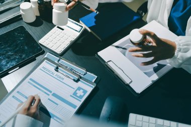 Two doctors and a female nurse meet at a table in the hospital, collaborating on medical tasks using laptops and computers