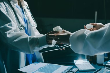 Two doctors and a female nurse meet at a table in the hospital, collaborating on medical tasks using laptops and computers