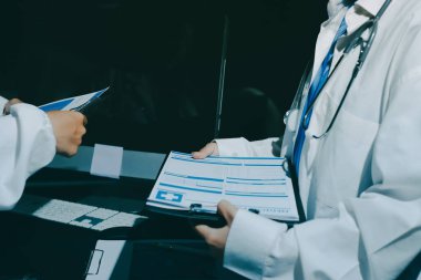 Two doctors and a female nurse meet at a table in the hospital, collaborating on medical tasks using laptops and computers