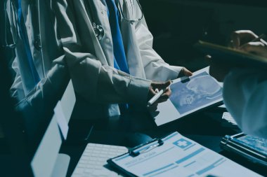 Two doctors and a female nurse meet at a table in the hospital, collaborating on medical tasks using laptops and computers