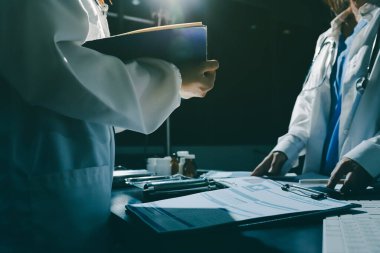 Two doctors and a female nurse meet at a table in the hospital, collaborating on medical tasks using laptops and computers