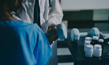 Fizyoterapist, halter egzersizinde bir kadına yardım ediyor.