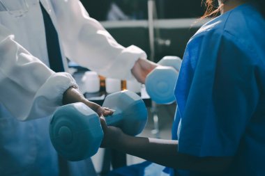 Fizyoterapist, halter egzersizinde bir kadına yardım ediyor.