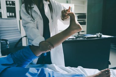 Hastane odasında yaralı bir kadının ayak bileğini inceleyen ve destekleyen doktor, burkulma ya da kırık için tıbbi yardım ve tedavi sunuyor.