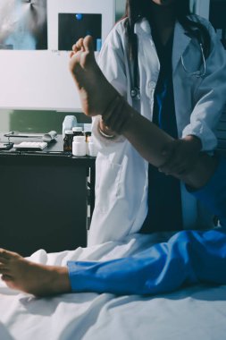 Hastane odasında yaralı bir kadının ayak bileğini inceleyen ve destekleyen doktor, burkulma ya da kırık için tıbbi yardım ve tedavi sunuyor.