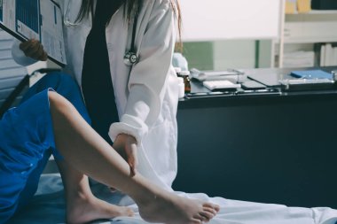 Hastane odasında yaralı bir kadının ayak bileğini inceleyen ve destekleyen doktor, burkulma ya da kırık için tıbbi yardım ve tedavi sunuyor.