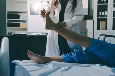 Hastane odasında yaralı bir kadının ayak bileğini inceleyen ve destekleyen doktor, burkulma ya da kırık için tıbbi yardım ve tedavi sunuyor.