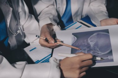 Two doctors and a female nurse meet at a table in the hospital, collaborating on medical tasks using laptops and computers