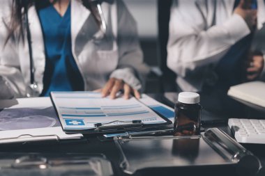 Two doctors and a female nurse meet at a table in the hospital, collaborating on medical tasks using laptops and computers
