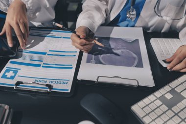 Two doctors and a female nurse meet at a table in the hospital, collaborating on medical tasks using laptops and computers