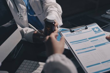 Two doctors and a female nurse meet at a table in the hospital, collaborating on medical tasks using laptops and computers