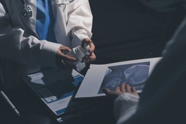 Two doctors and a female nurse meet at a table in the hospital, collaborating on medical tasks using laptops and computers