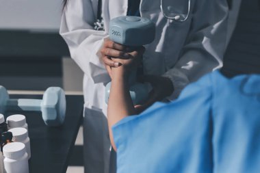 Fizyoterapist, halter egzersizinde bir kadına yardım ediyor.