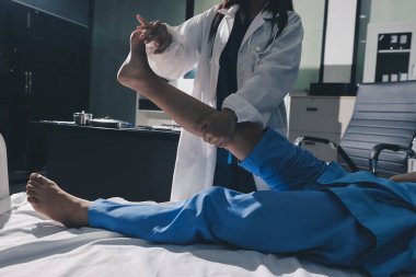 Hastane odasında yaralı bir kadının ayak bileğini inceleyen ve destekleyen doktor, burkulma ya da kırık için tıbbi yardım ve tedavi sunuyor.