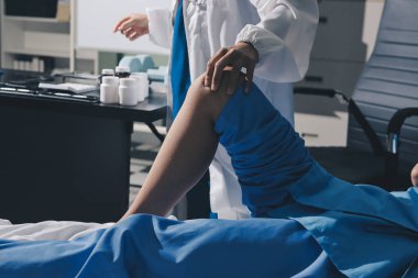 Hastane odasında yaralı bir kadının ayak bileğini inceleyen ve destekleyen doktor, burkulma ya da kırık için tıbbi yardım ve tedavi sunuyor.