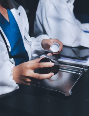Two doctors and a female nurse meet at a table in the hospital, collaborating on medical tasks using laptops and computers