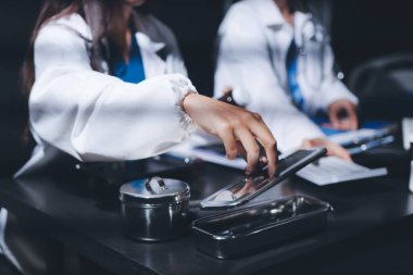 Two doctors and a female nurse meet at a table in the hospital, collaborating on medical tasks using laptops and computers