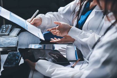 Two doctors and a female nurse meet at a table in the hospital, collaborating on medical tasks using laptops and computers
