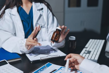 Two doctors and a female nurse meet at a table in the hospital, collaborating on medical tasks using laptops and computers