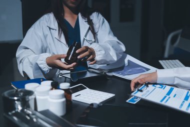 Two doctors and a female nurse meet at a table in the hospital, collaborating on medical tasks using laptops and computers
