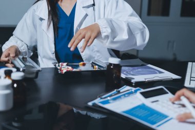 Two doctors and a female nurse meet at a table in the hospital, collaborating on medical tasks using laptops and computers