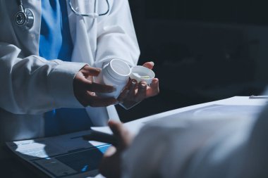 Two doctors and a female nurse meet at a table in the hospital, collaborating on medical tasks using laptops and computers
